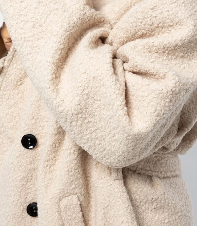 Detailansicht eines beigen Mantels mit Knöpfen und texturiertem Stoff für gemütlichen Style.