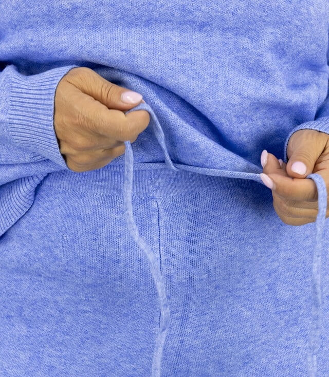 Detailansicht des Strick Zweiteilers in hellblau. Modell zieht an den Schnüren der hellblauen Sweathose