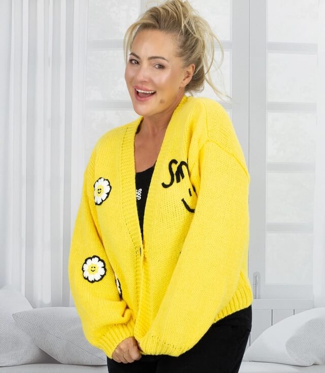 Lässiger gelber Strickcardigan mit Blumen und Smiley-Details, von einer Model getragen.