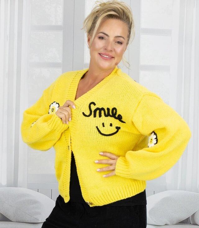 Helle gelbe Strickjacke mit lächelndem Smile-Print und Blumenmuster, lässig getragen von einer Frau.