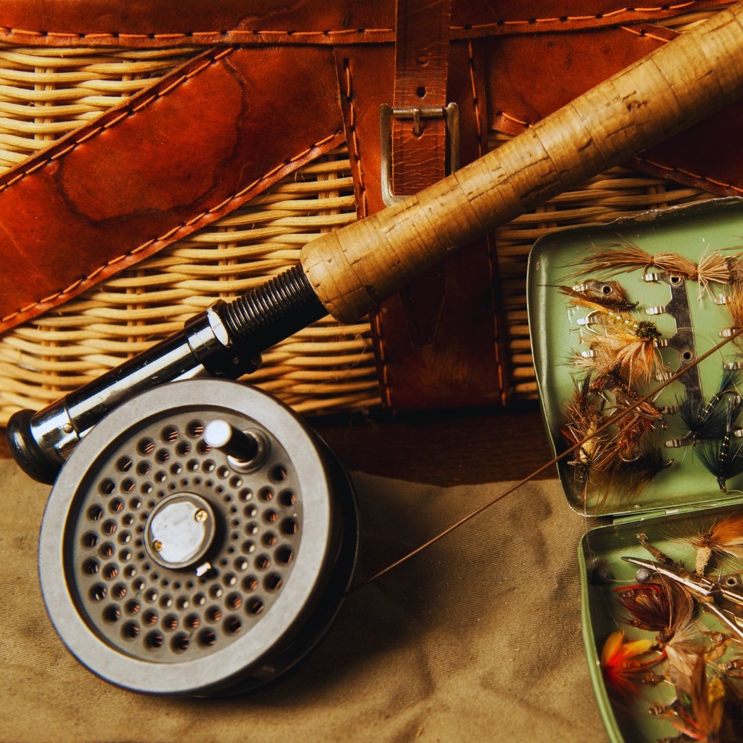 Classic fly fishing gear—rod, reel, fly box, and wicker creel—arranged as a still life.