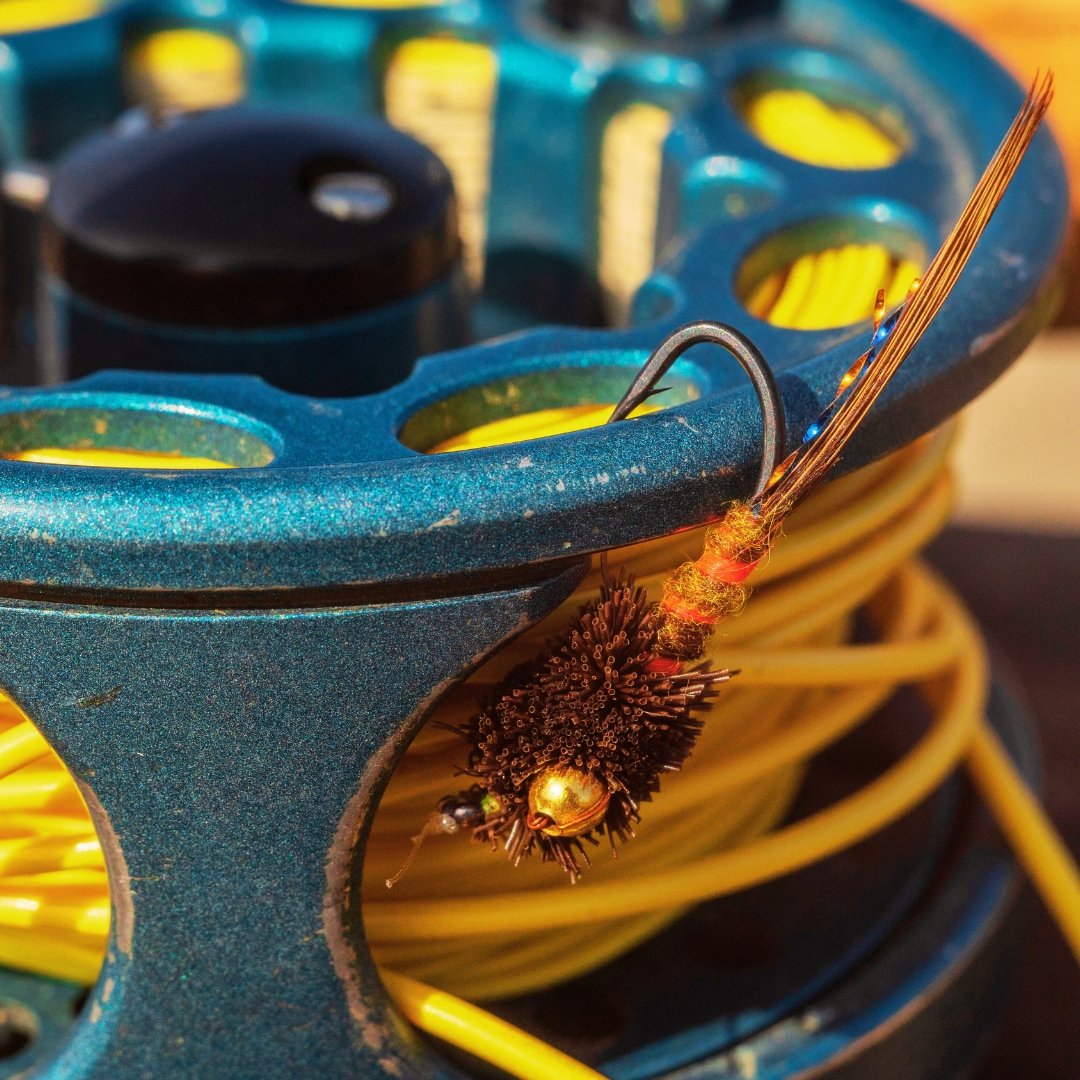 Close-up of a fly reel with fly line and a single fly hanging off the reel’s edge.