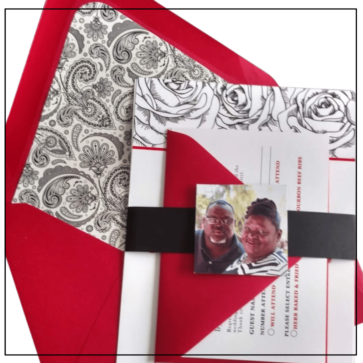 A bespoke wedding invitation suite by SaKredJoi Art featuring a vibrant red envelope with a black and white paisley liner. The suite includes a coordinated RSVP card and a custom photo belly band, showcasing high-end artisan paper art designed as a lasting keepsake.