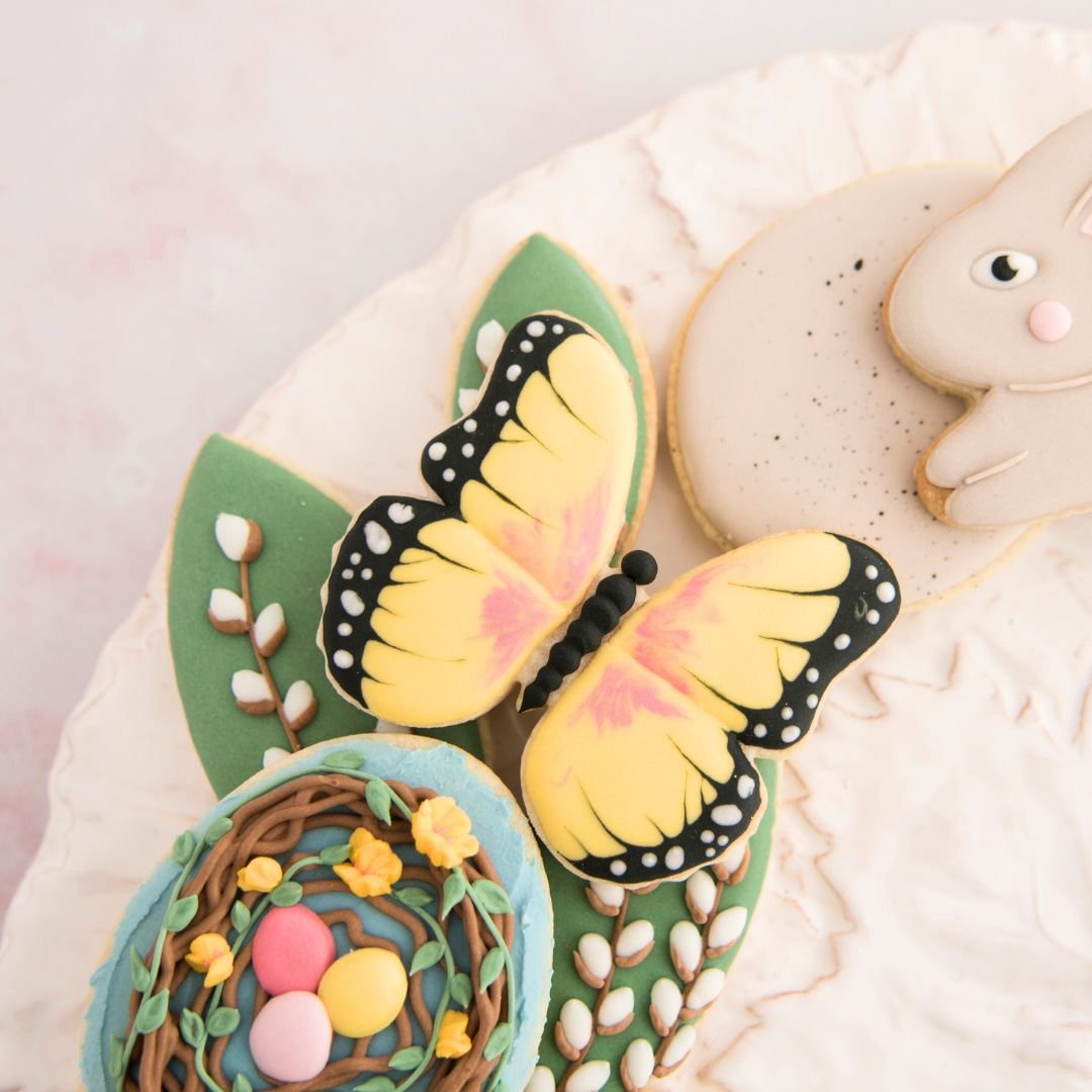 Cookie in a shape of a butterfly decorated with icing on a plate.