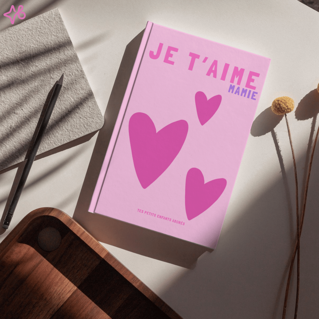 Maquette réaliste de lalbum photo personnalisé Je taime Mamie rose sur une table avec carnet, crayon et fleurs séchées. Lumière douce et ombre portée élégante. Cadeau mémorable.