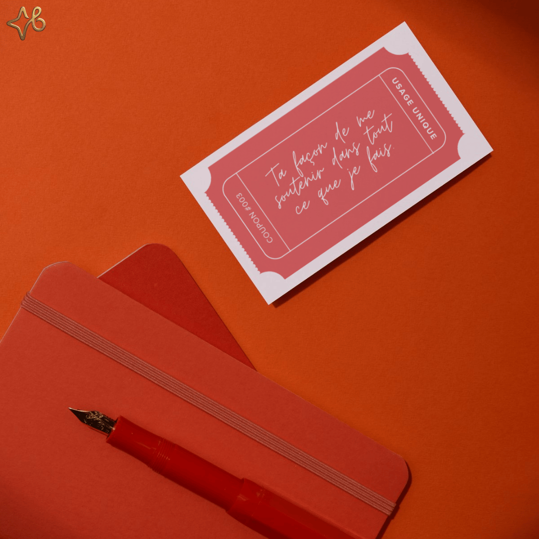 Coupon de message doux posé à côté d'un carnet rouge et d'un stylo plume, illustrant l'aspect personnalisable et fait main du cadeau.