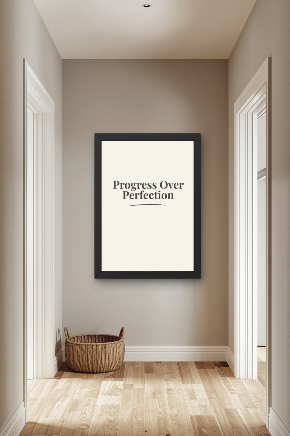 A charcoal typographic wall art print in a black frame centered on a warm taupe hallway wall between two white-trimmed doorways with a wicker basket on warm wood floorboards below and recessed ceiling light above.