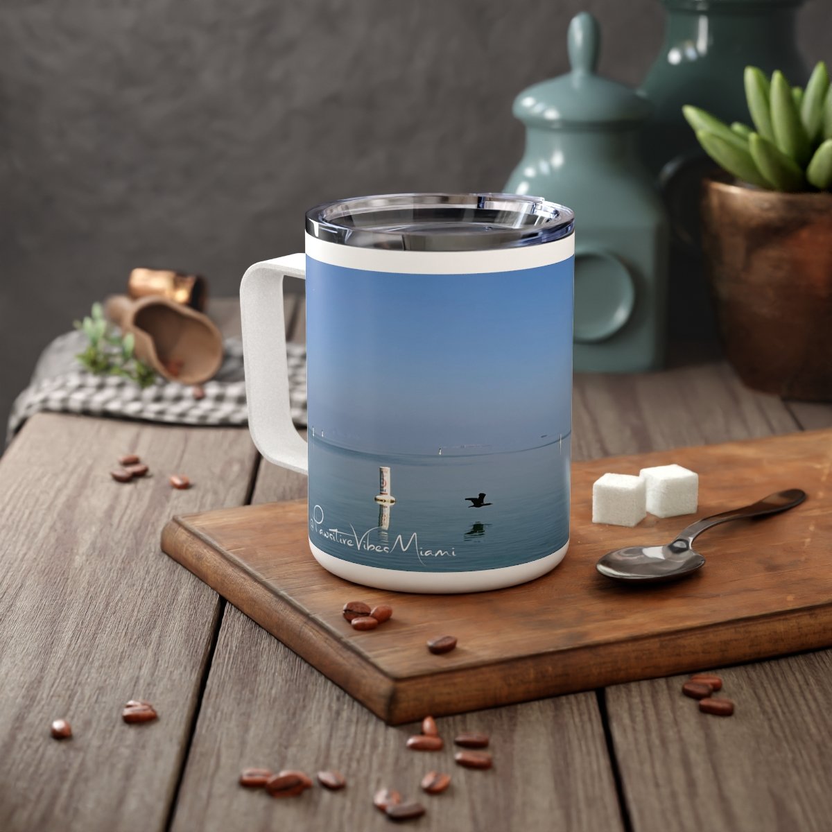 “Front view of insulated stainless steel mug featuring a warm Miami sunrise over the water.”