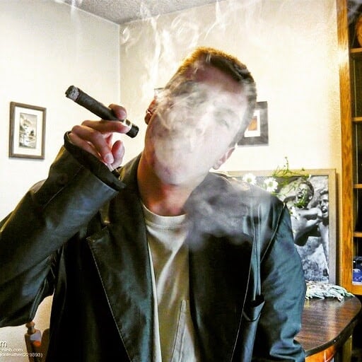 Oregonleatherboy sporting black leather blazer blowing out gar smoke holding long brown cigar with crew cut