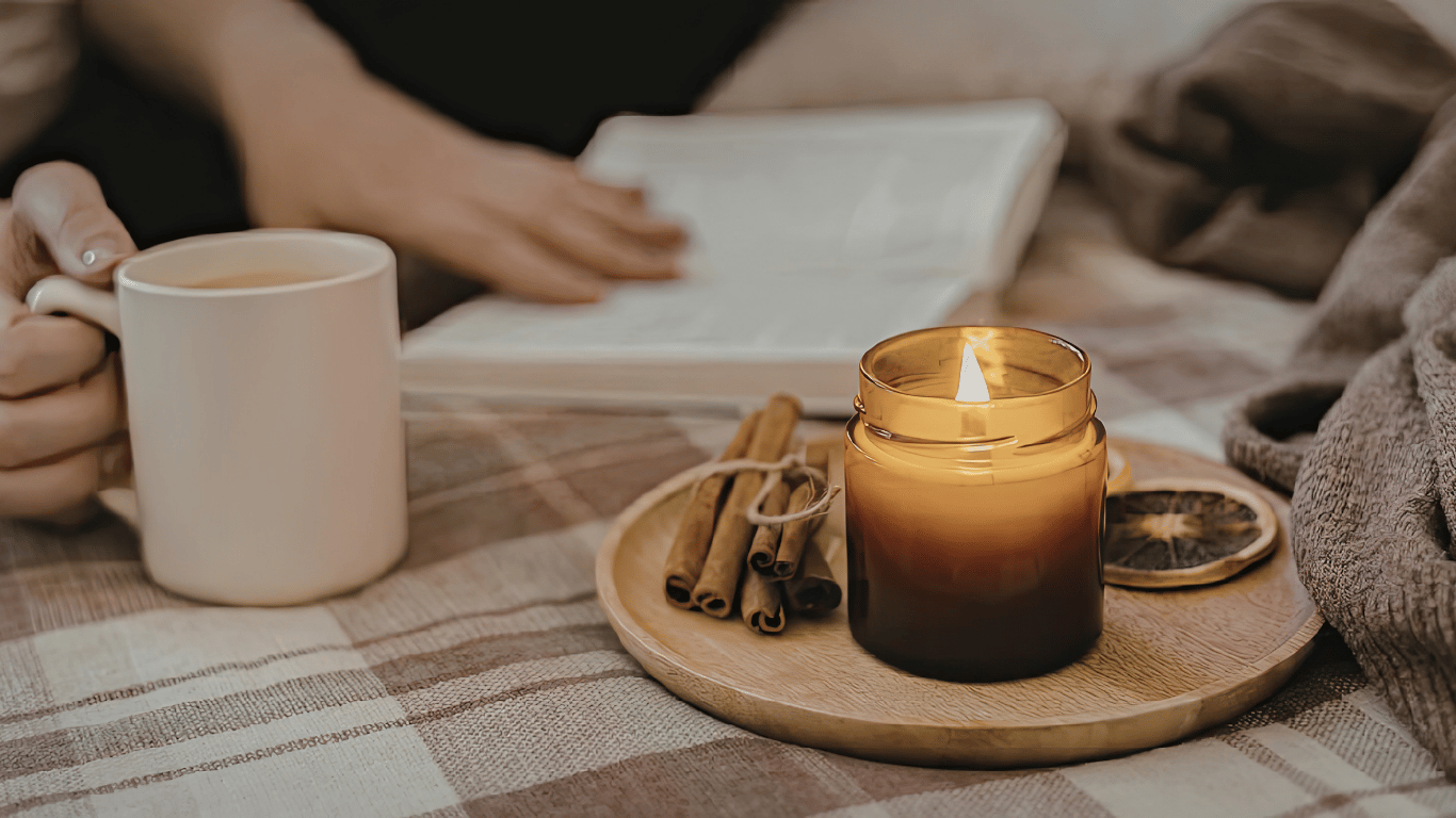 Woman relaxing with a warm cup of tea, lit candle, cinnamon sticks and a book — cosy self-care and personal wellness lifestyle