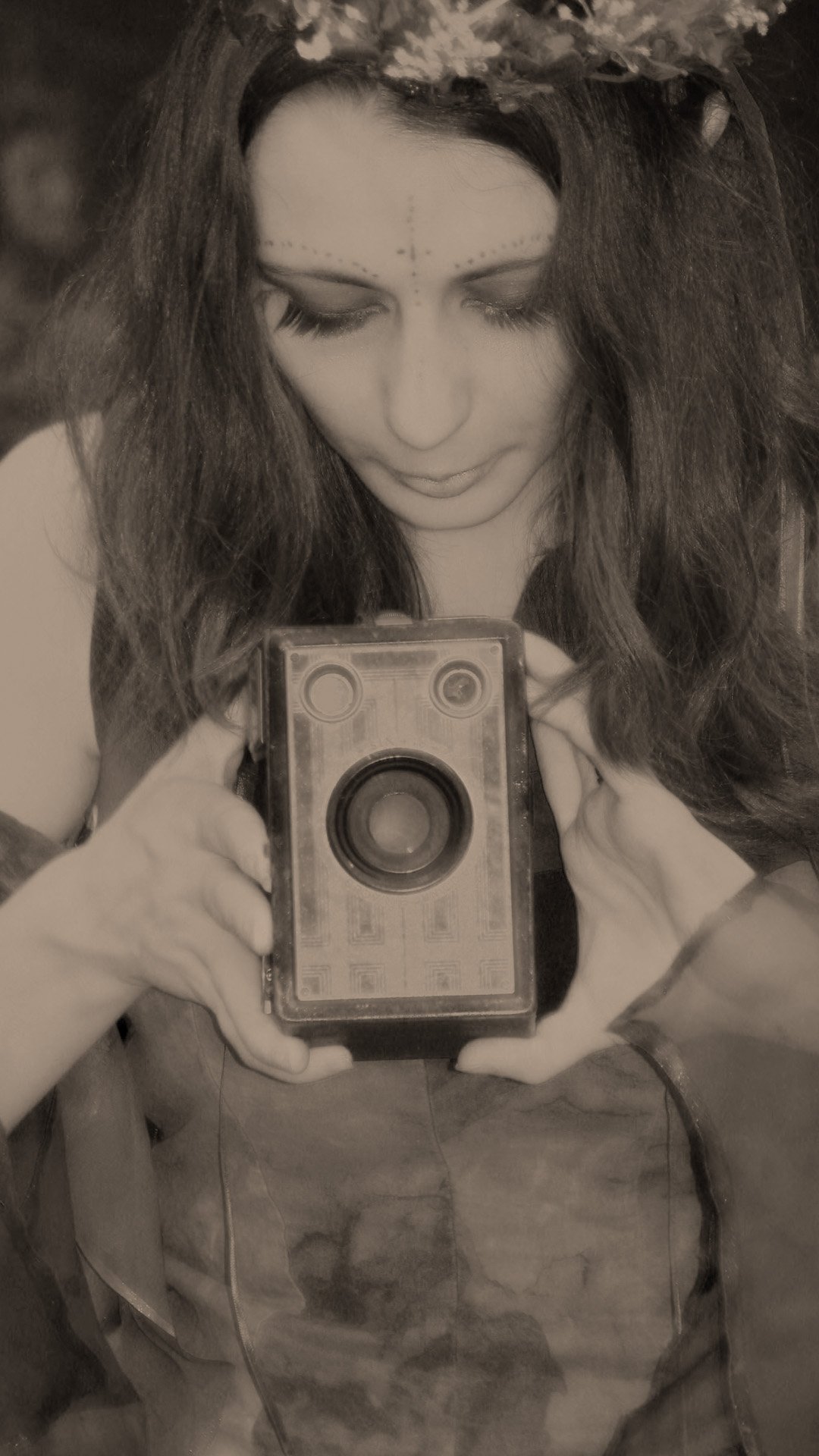 Sepia toned image of a fairy pointing an old brownie camera at the viewer.