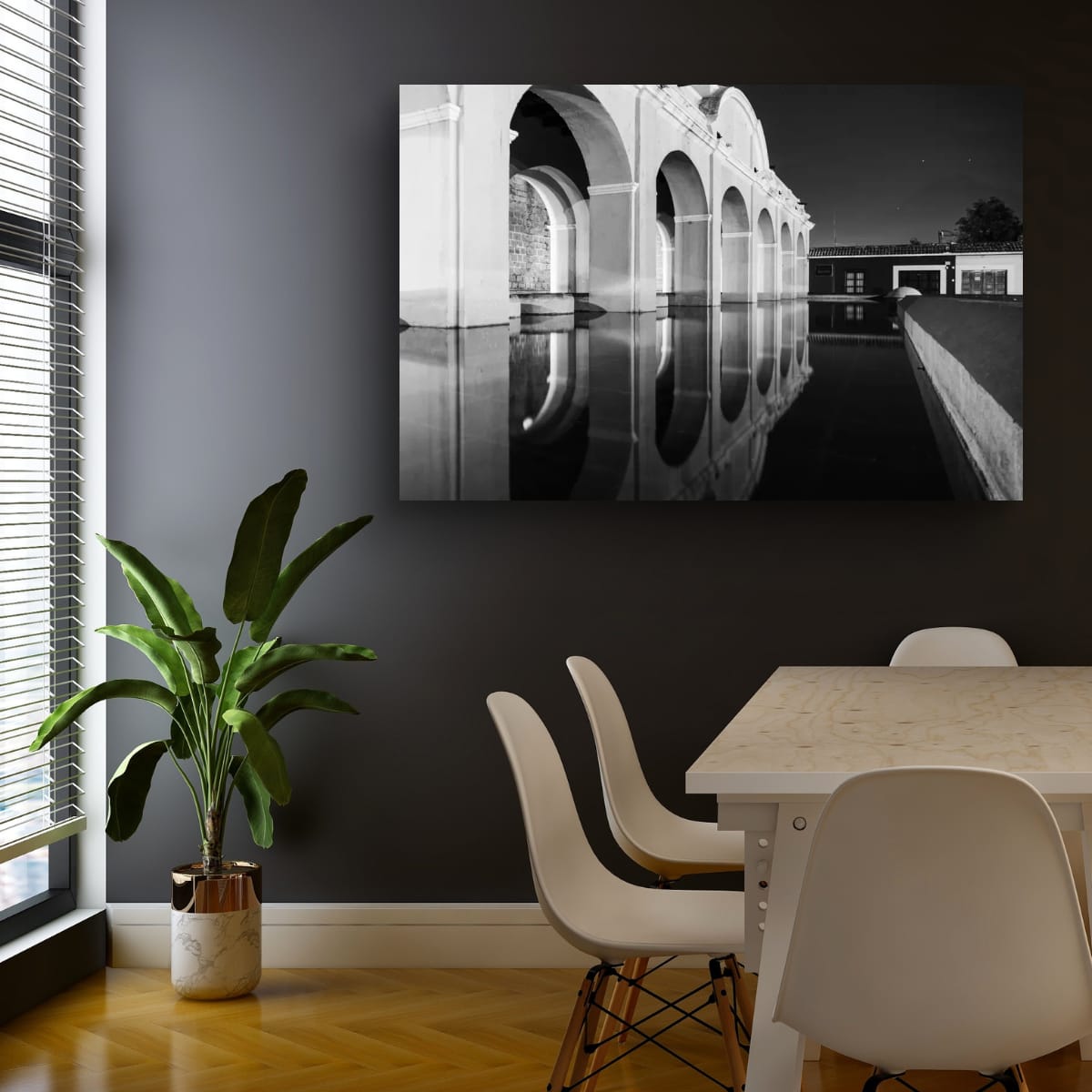 A horizontal black and white photograph of the neoclassical arches of the Tanque de la Union in Antigua, Guatemala, reflecting perfectly in a still pool of water at night.