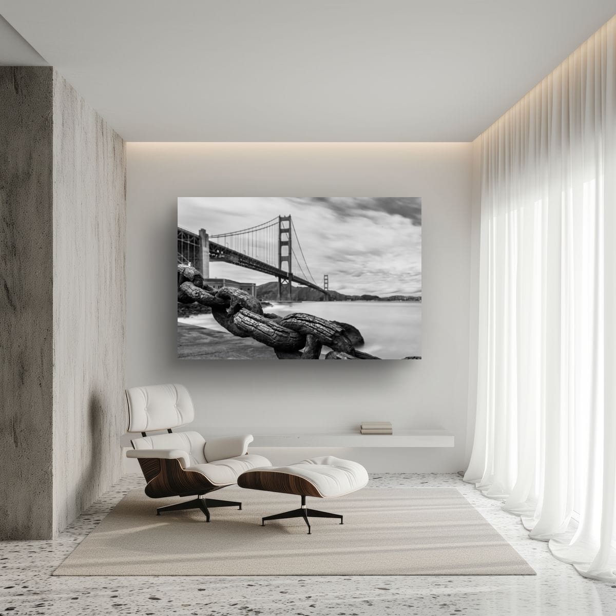 A large horizontal canvas print of a black and white long-exposure bridge photograph hangs on a white living room wall above a white leather lounge chair and ottoman.