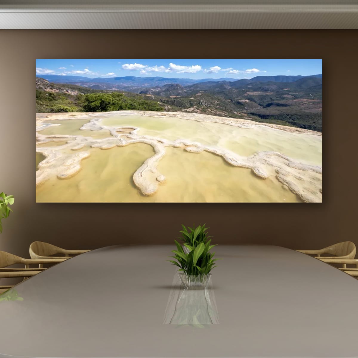 A large frameless panoramic canvas print of Hierve el Agua hangs on a minimalist brown boardroom wall over a sleek conference table with a potted plant centerpiece
