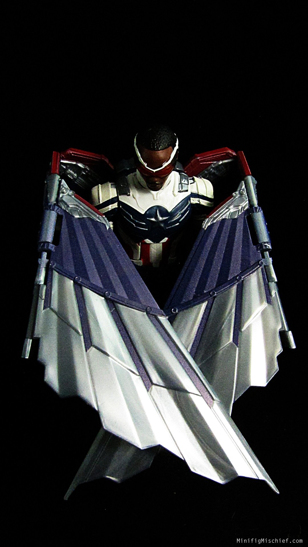 pic of sam wilson action figure. his wings are folded in front of him and his head is bowed. hes in front of a black background.