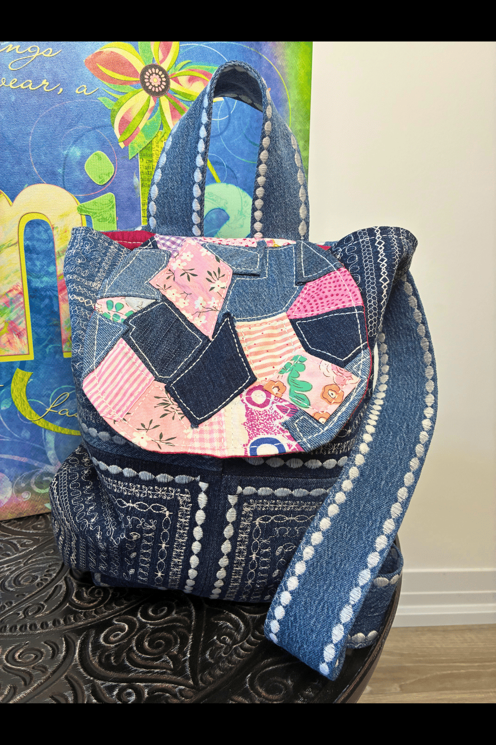 Front view of a handmade patchwork backpack featuring a scrappy fabric flap made from mixed denim and patterned fabric scraps with visible stitching and textured details throughout.
