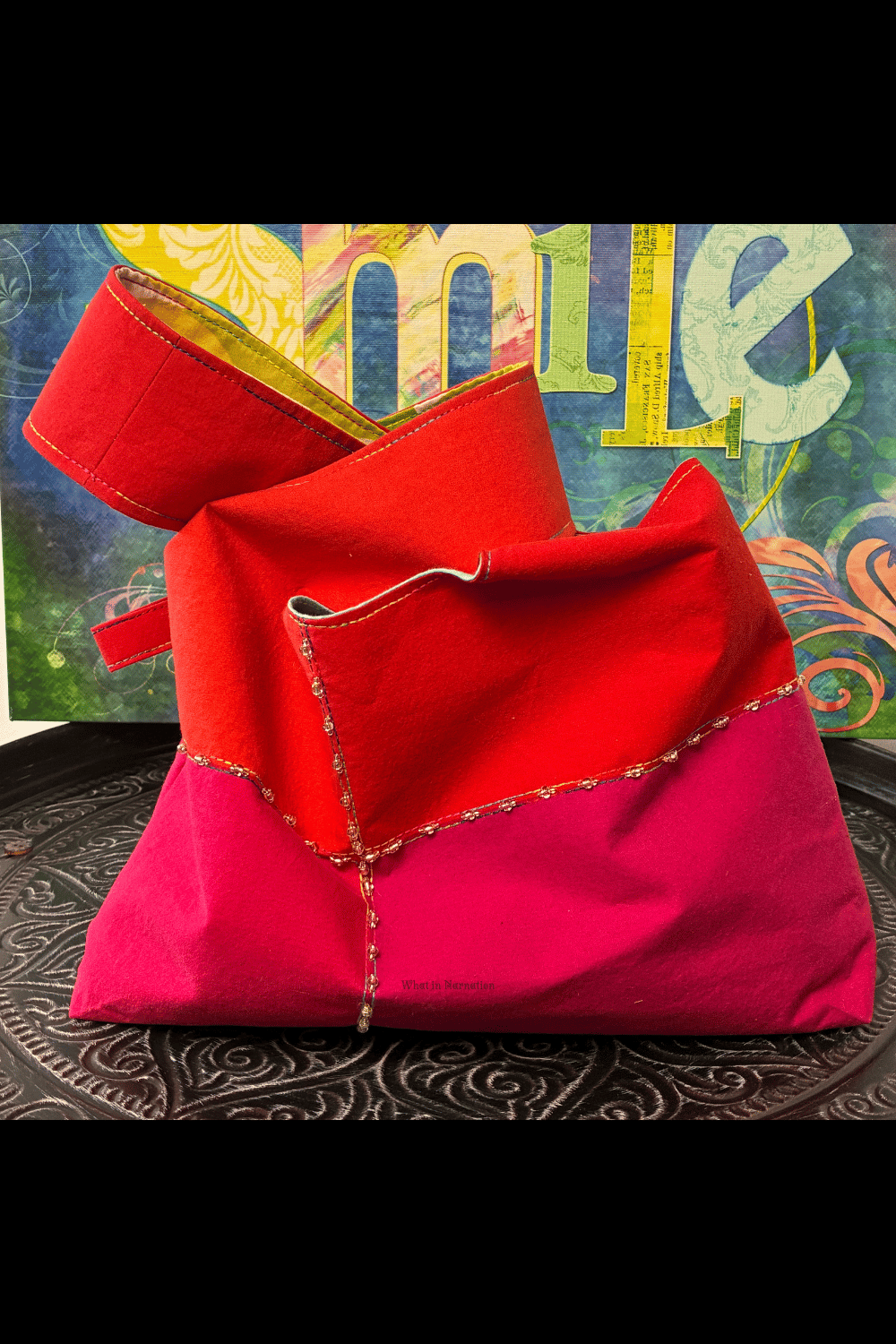 Front view of a handmade upcycled knot bag featuring bold hot pink and orange colour blocking, decorative rainbow stitching, and hand-sewn bead details.