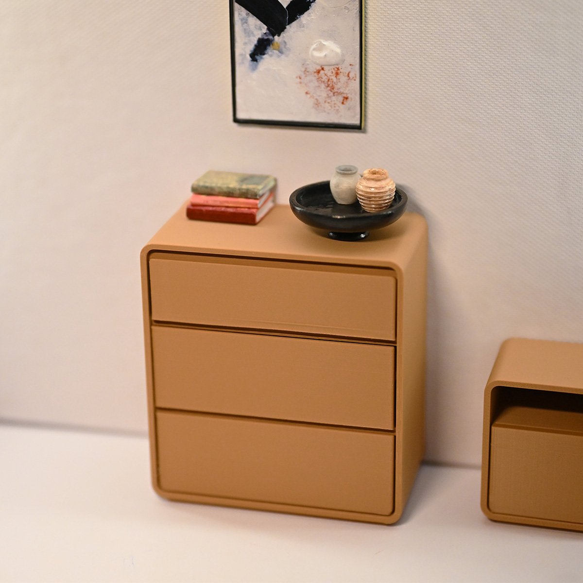 A roombox with the dresser and various accesories on top and a painting on the wall