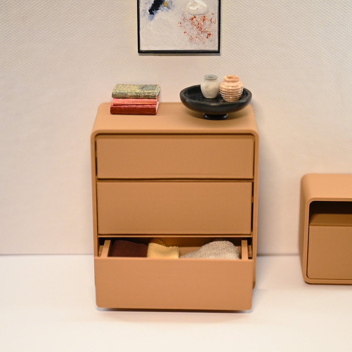 A roombox with the dresser and various accesories on top and a painting on the wall