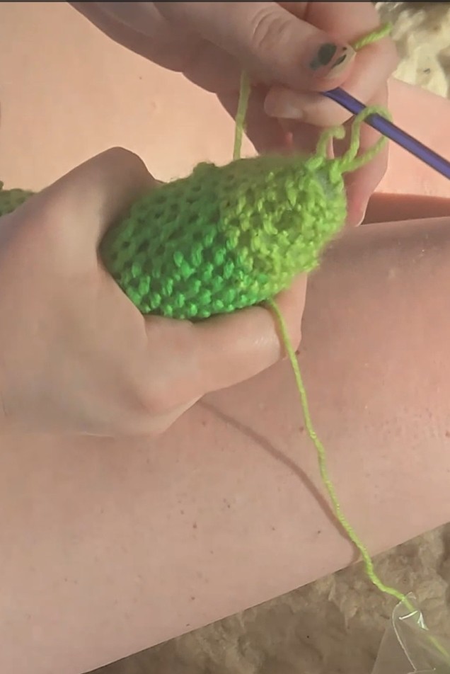 a person crocheting a pickle amigurumi