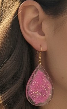 Close-up of handmade pink glitter resin teardrop earring being worn