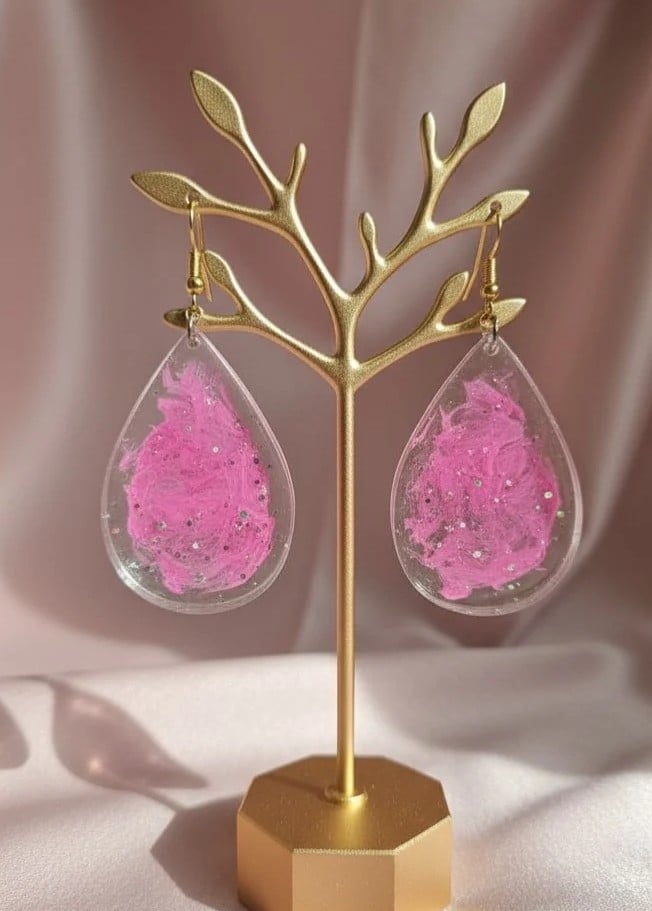 Pair of handmade pink glitter resin teardrop earrings displayed on a gold jewellery stand