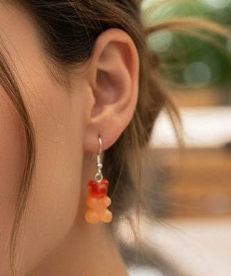 Close-up of red orange and peach gummy bear resin drop earring being worn