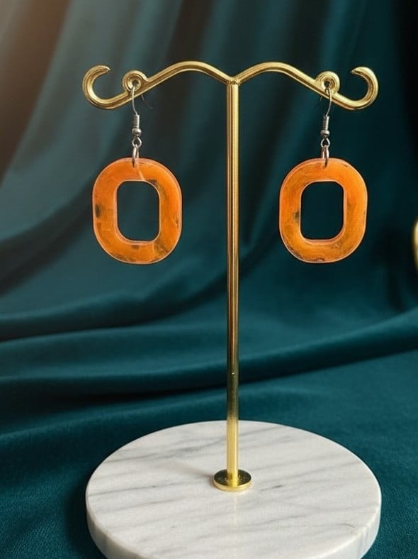 Handmade orange marbled resin open-oval drop earrings displayed on a gold jewellery stand