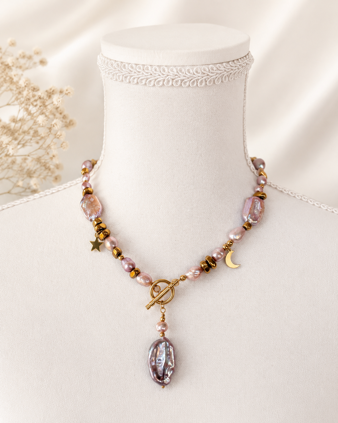 Collana artigianale con perle d’acqua dolce rosa, perla barocca, ematite dorata e chiusura T-Bar su manichino beige.