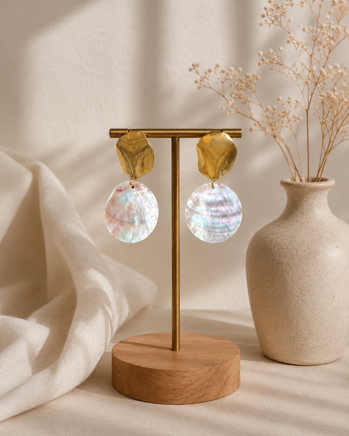 Orecchini artigianali in madreperla naturale con base in acciaio inox color oro, esposti su supporto dorato con sfondo chiaro in stile minimal.