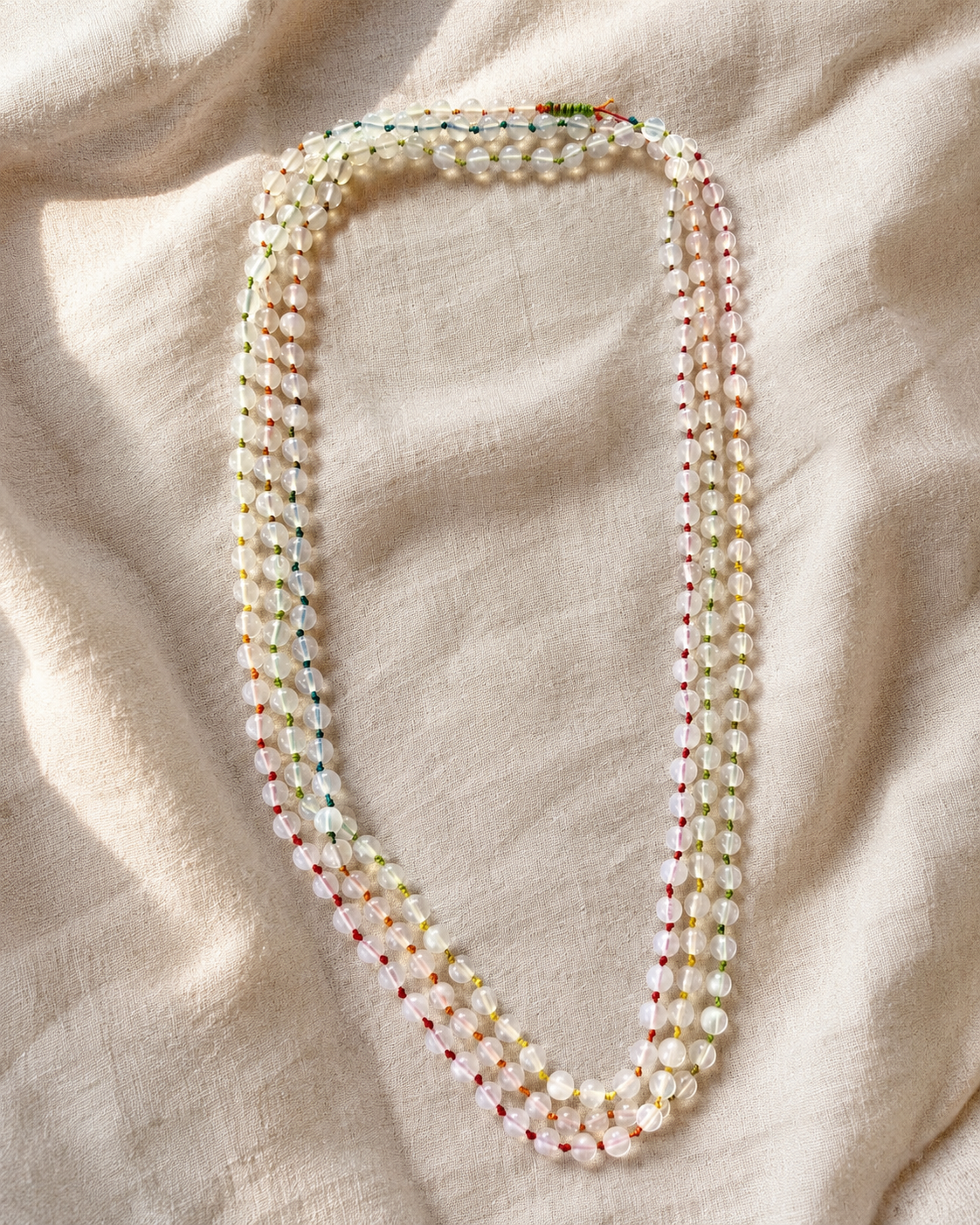 Collana in pietra di luna naturale da 4 mm con filo colorato fotografata su tessuto chiaro.