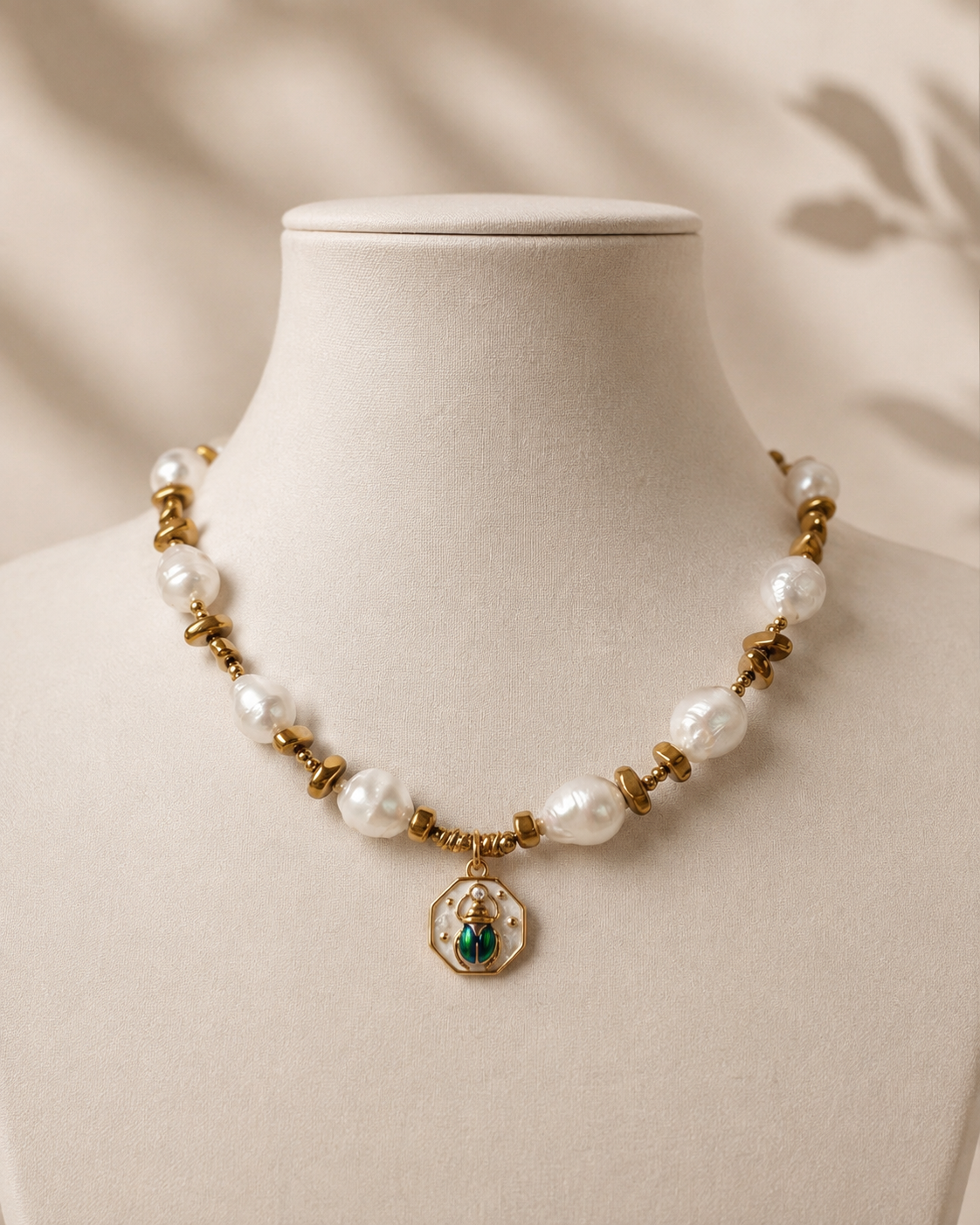 Collana con perle barocche, ematite color oro e pendente scarabeo su manichino.