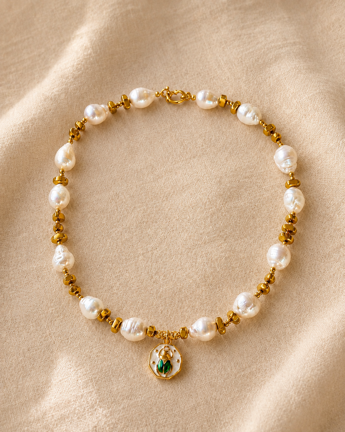 Collana artigianale con perle naturali, ematite color oro e pendente scarabeo su sfondo chiaro.