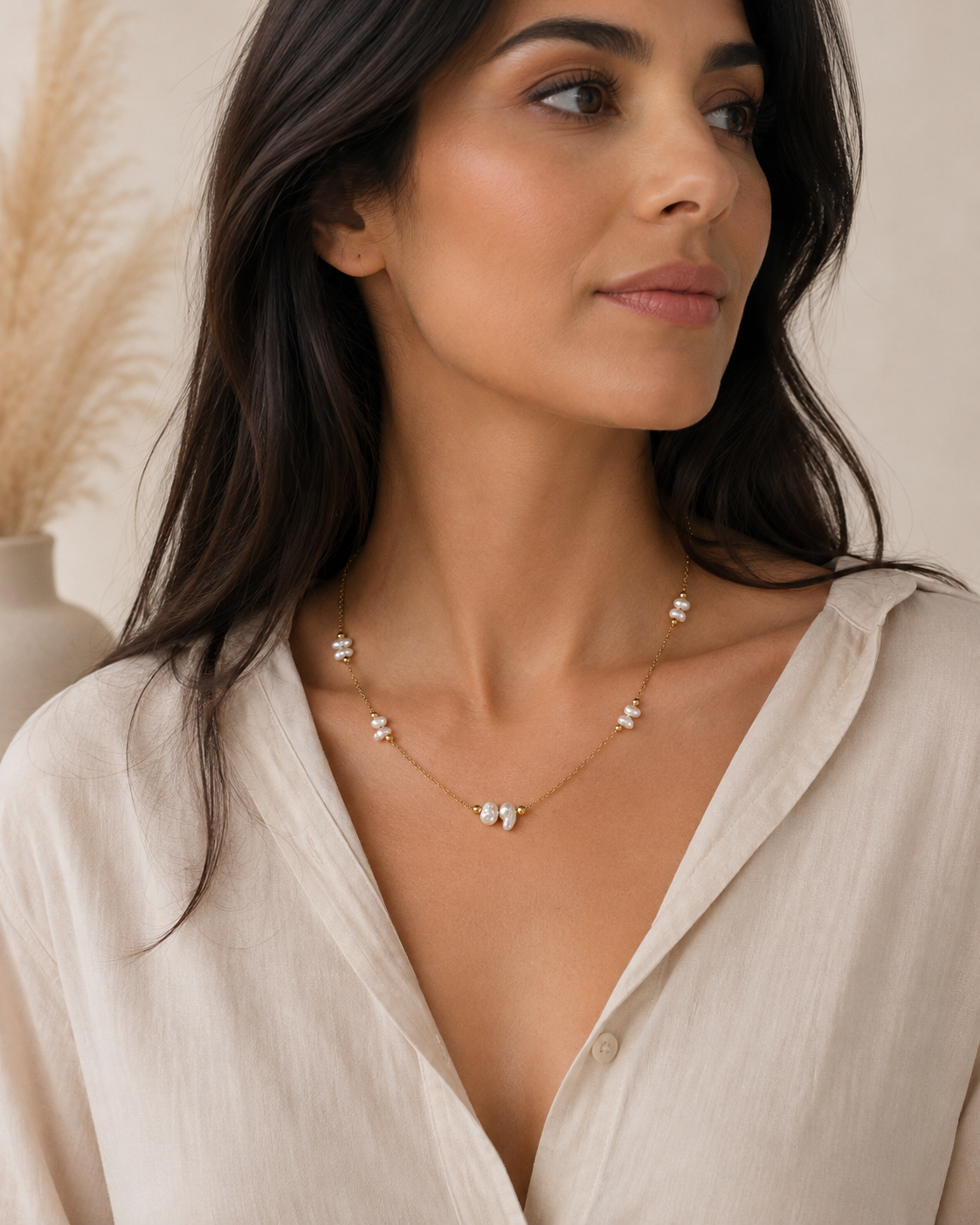 Donna che indossa una collana minimal in acciaio color oro con perle di fiume naturali.