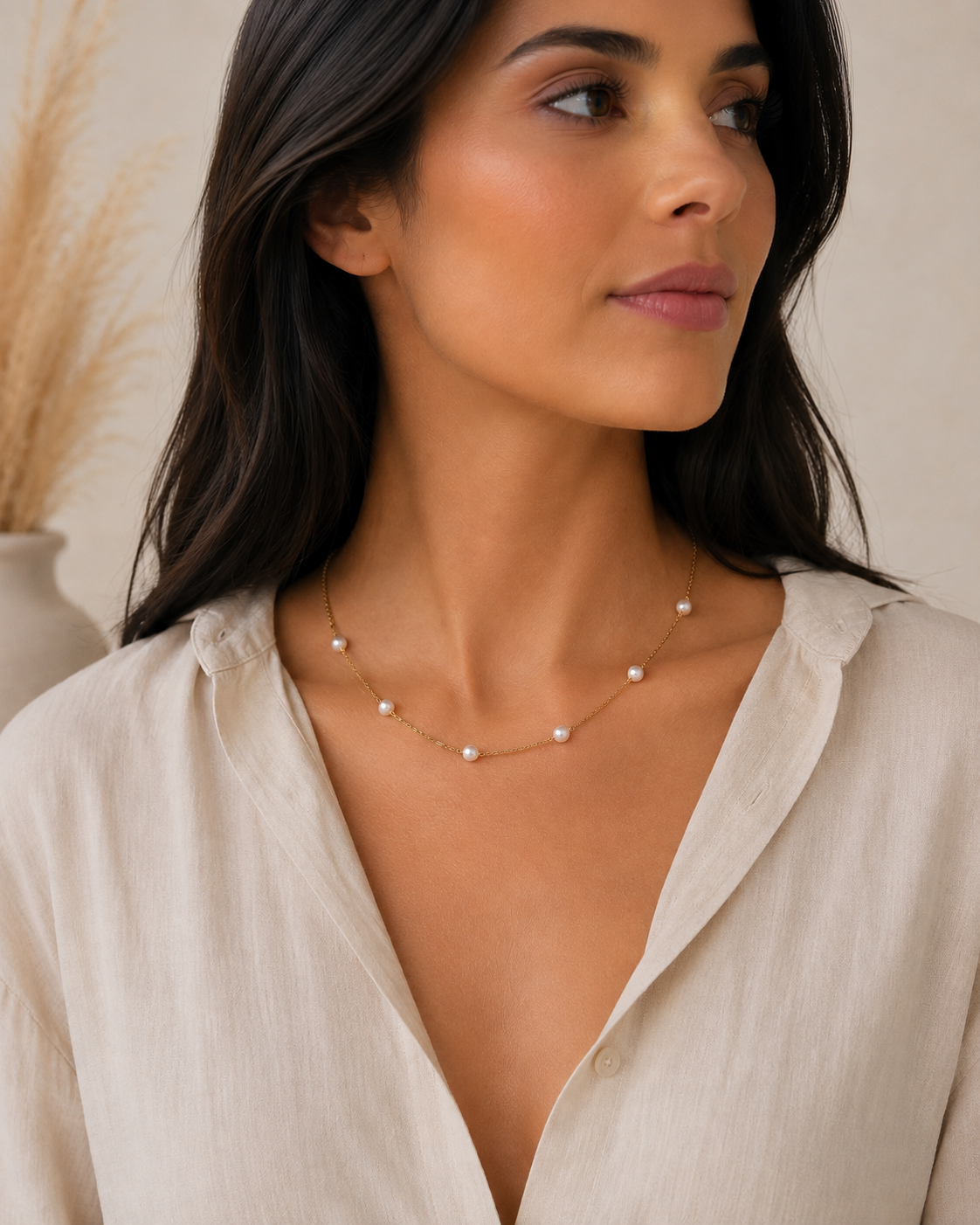 Donna che indossa una collana minimal in acciaio color oro con perle di fiume naturali.