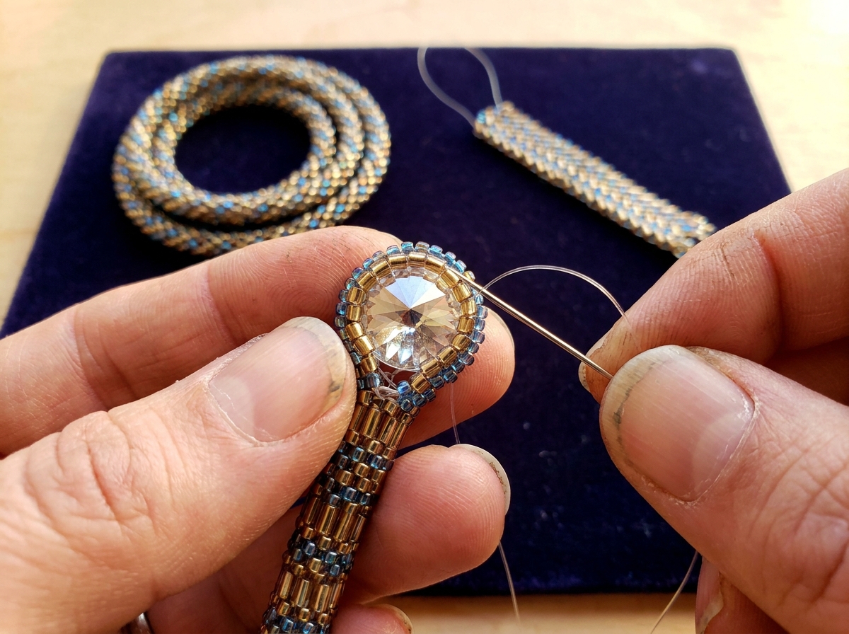 Close-up of hands weaving tubular peyote stitch around a faceted rivoli crystal to create an open-back beaded bezel, demonstrating the core beadwork techniques used in crystal jewelry making.