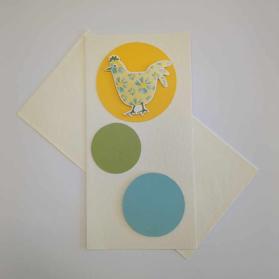 A tall cream greetings card with a matching cream envelope. Three circles in different colours and sizes bubble up the length of the card. The bottom circle is turquoise blue, the middle is smaller and green, the top one is yellow and has a motif of a chi