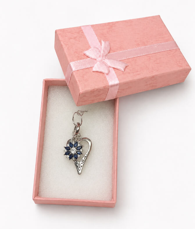 Handmade 925 sterling silver bridal bouquet memory charm featuring a sapphire blue crystal sunburst cluster inside an open filigree silver heart pendant inside an open pink gift box.
