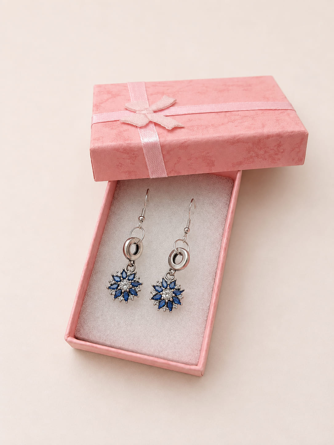 Handmade 925 sterling silver bridal drop earrings featuring a brilliant blue and clear crystal sunflower burst charm inside a textured pink gift box.