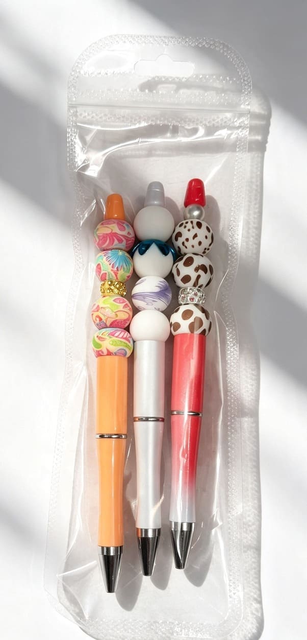A curated three-pack collection of custom patterned silicone beaded pens sealed inside a clear cellophane retail display hang-bag with a built-in resealable strip.