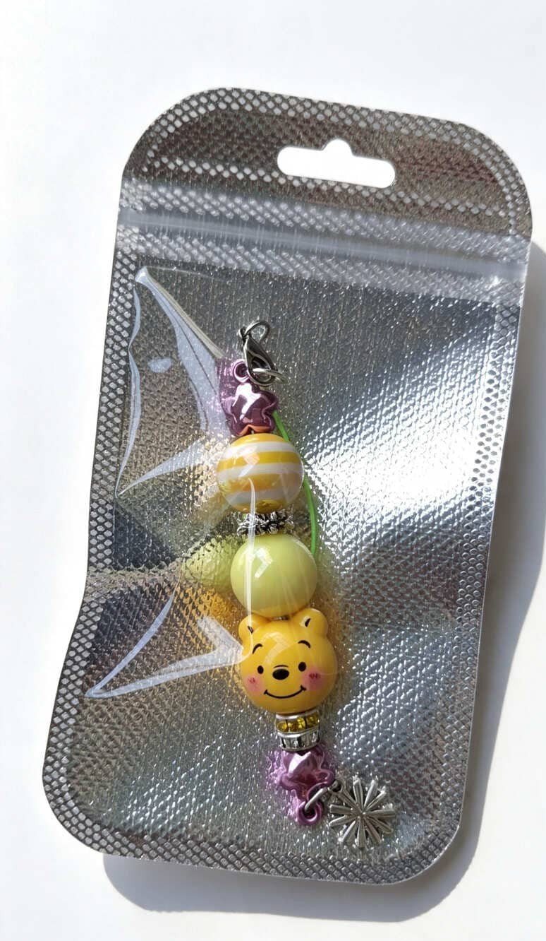 Bright and Cheerful Yellow Bear Pastel Phone Charm from Sparkling Resin Delights, securely packed inside a clear-fronted silver holographic display bag with a retail hang hole.