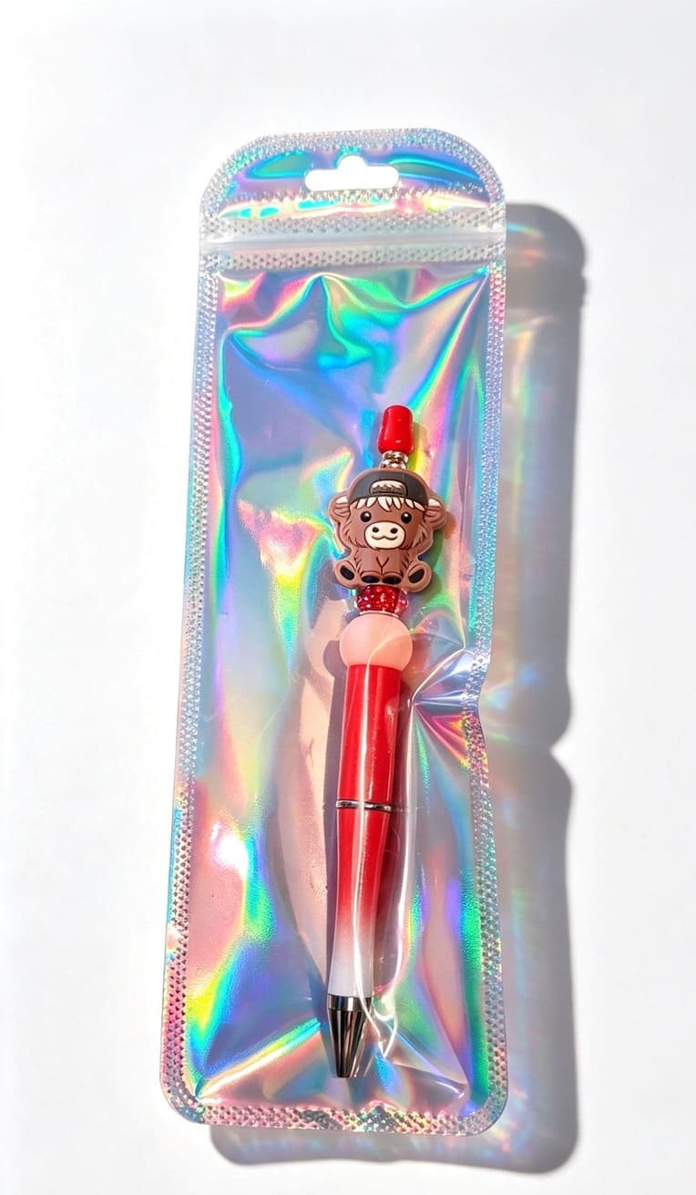 The red sparkle baseball cap Highland cow novelty pen showcased inside a retail-ready silver holographic ziplock display bag.
