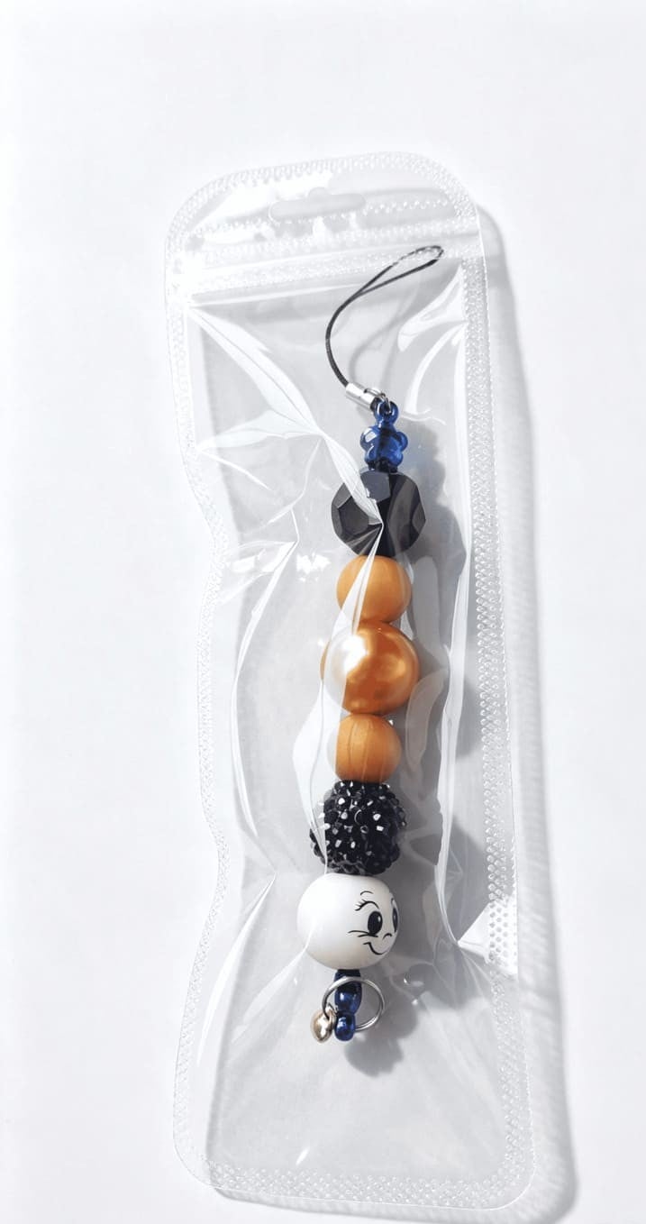 Handmade orange and black smiley face beaded phone strap presented in a clear protective resealable pouch