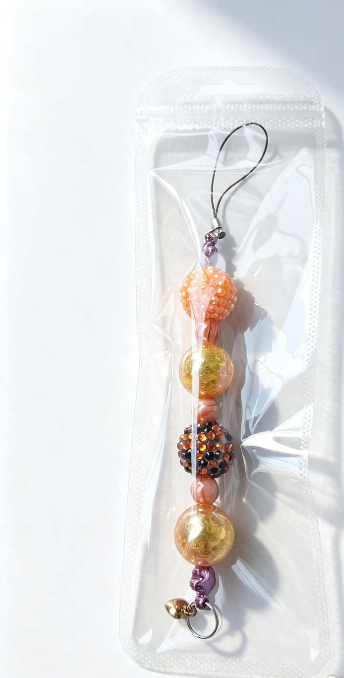 Handmade orange rhinestone and gold foil beaded phone charm presented in a clear protective resealable pouch