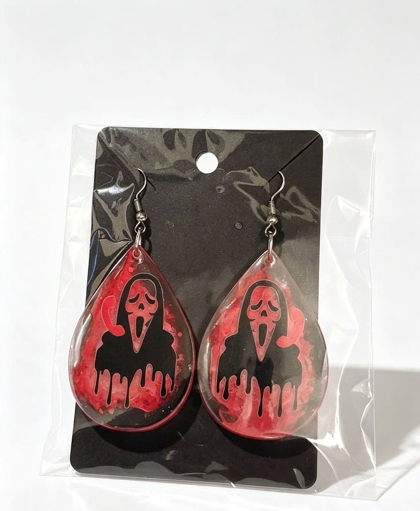 Handmade horror teardrop earrings with black and red Ghostface-style design packaged on a black display card
