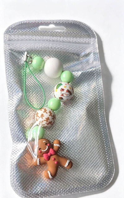 Handmade Gingerbread Christmas beaded holiday ornament charm by Sparkling Resin Delights, safely showcased inside its clear boutique packaging with a sparkling silver foil background. The vertical bead stack and smiling clay gingerbread man charm are neat