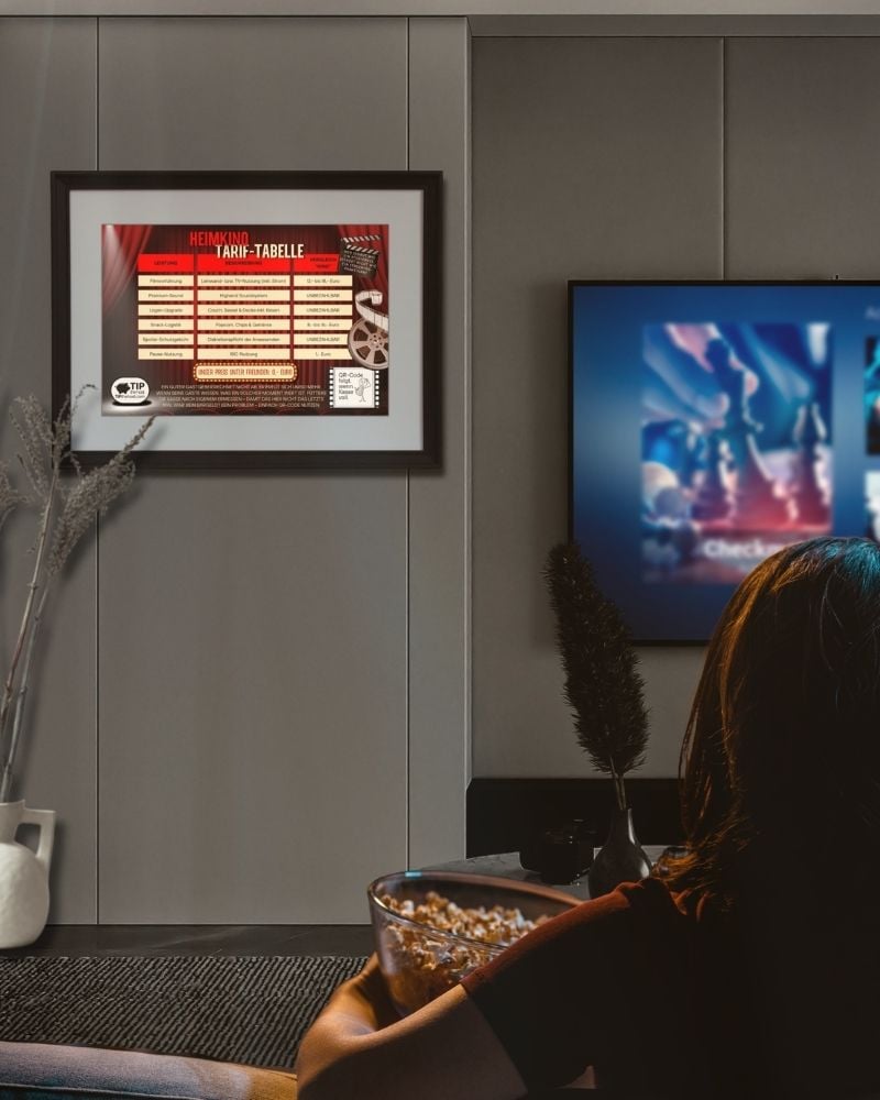 Frau mit Popcornschale vor der gerahmten Preisliste fürs Heimkino, Tarif-Tabelle neben dem Fernseher an der Wand