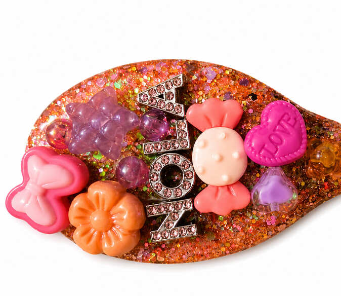Close-up of personalised resin hairbrush with glitter, rhinestone-style name, bow, flower, heart and sweet charms