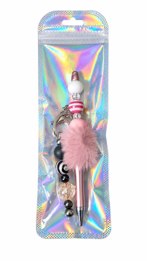 A dusty rose pom-pom beaded pen and dark gunmetal heart keychain set displayed inside a glossy, iridescent holographic retail pouch.