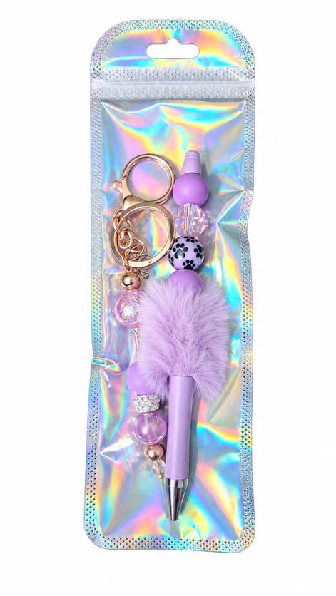 A deep violet pom-pom beaded pen and matching rose gold keychain set displayed inside a glossy, iridescent holographic retail pouch.